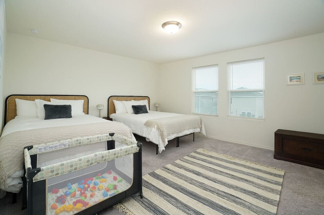 A bedroom with two beds, a crib, a striped rug, and a dresser.