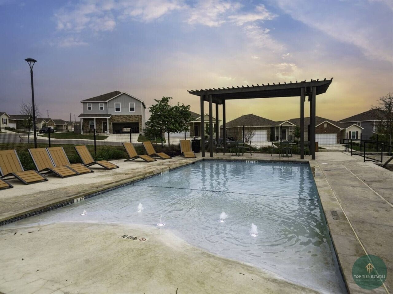 Piscina com espreguiçadeiras e pérgola, cercada por casas.