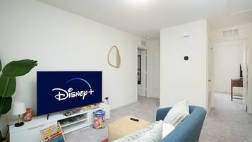 Ein Wohnzimmer mit einem Flachbildfernseher, der das Disney+-Logo zeigt, einem blauen Sofa, einem kleinen Couchtisch und einer Pflanze.