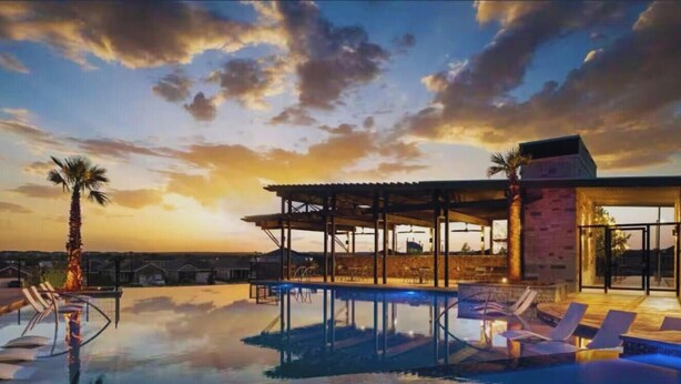 Ein Pool auf dem Dach mit Liegestühlen und einer überdachten Sitzgruppe, mit Blick auf die Skyline der Stadt bei Sonnenuntergang.