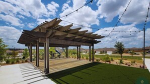 Ein überdachter Außenbereich mit einer Pergola, künstlicher Beleuchtung und einem gepflegten Rasen.