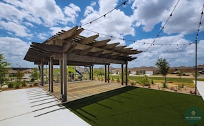 An outdoor patio with a pergola structure, artificial grass, and a playground in the background. - Rare Find Sleeps 13 Family Fun (San Antonio)