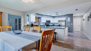 Une cuisine moderne avec des meubles blancs, un îlot central et un coin repas comprenant une table et des chaises.