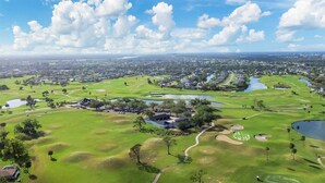 Vue aérienne d’un parcours de golf comportant plusieurs trous, avec des plans d’eau et des zones résidentielles en arrière-plan.