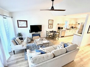 A modern living room with a sofa, coffee table, and TV, a dining area with chairs, and a kitchen with appliances. - Tranquil Oasis Golf Course Views Near Beach 1809 (Seabrook Island)