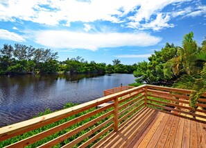 Une terrasse en bois surplombant une rivière paisible, avec une végétation luxuriante et des arbres en arrière-plan.
