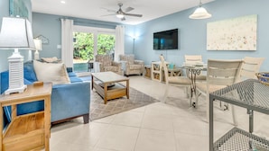 A spacious living room with a blue sofa, patterned armchairs, a coffee table, and a dining area with a table and chairs. - Somewhere in the Sun (Santa Rosa Beach)