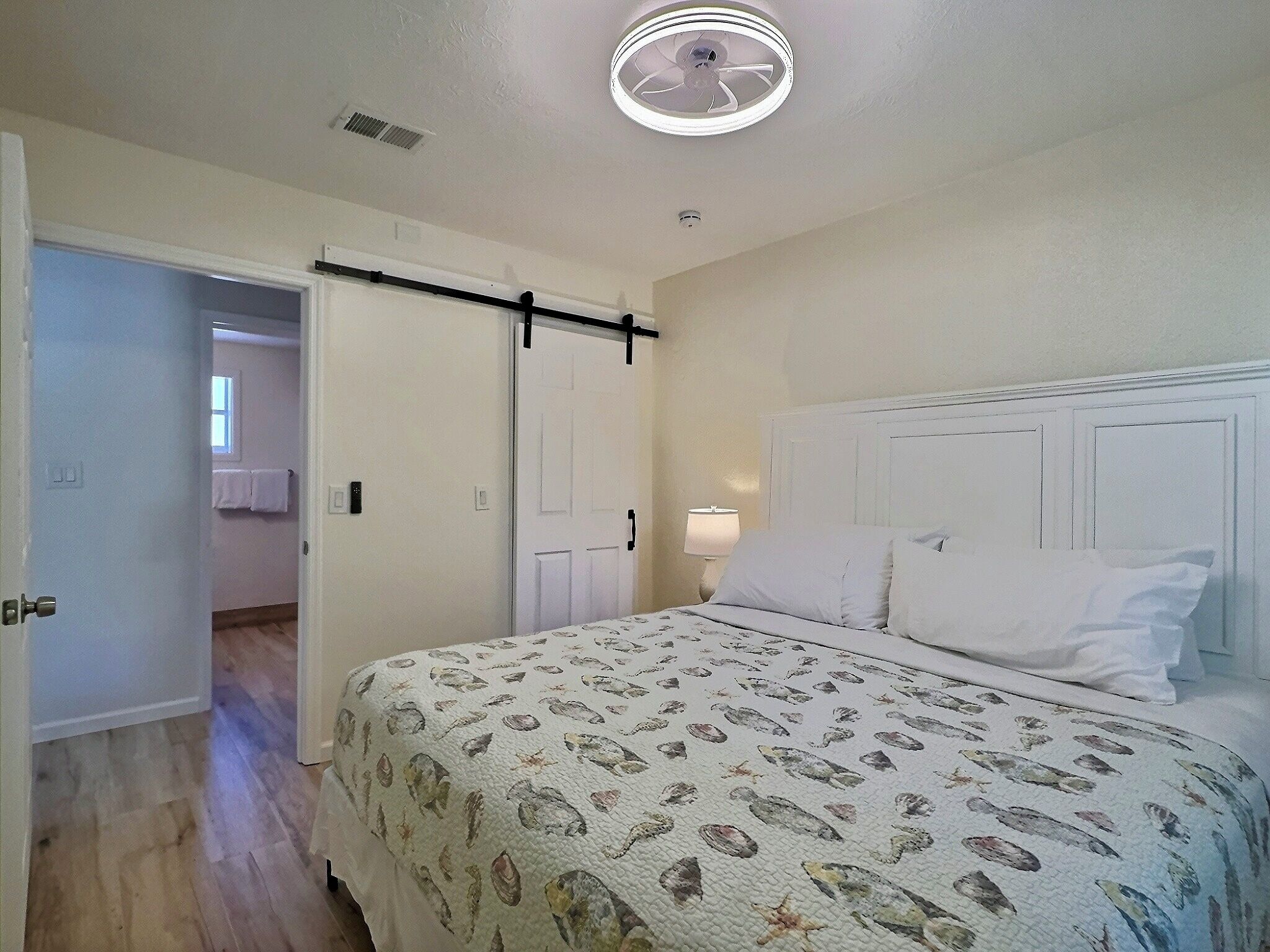 A bedroom with a bed, a nightstand, a ceiling fan, and a door leading to another room.