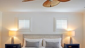 A bedroom with a wooden headboard, two bedside tables with lamps, and two windows with blinds. - The Treehouse (Siesta Key)