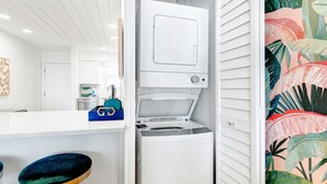 A compact kitchen with a built-in washer and dryer, a blue storage box, and a dark blue bar stool. - Seagroovy (Santa Rosa Beach)