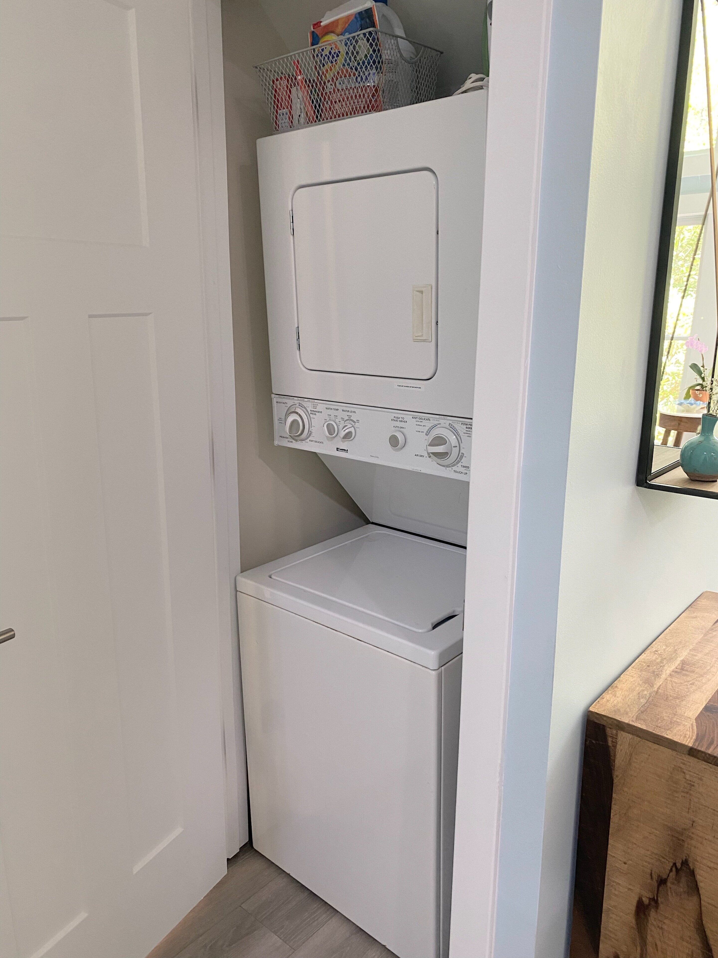 Een kleine wasruimte met een voorlader wasmachine en droger, een klein raam en een houten bankje.