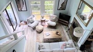 Un loft espacioso con techos altos, un ventanal grande, un ventilador de techo y una zona de estar acogedora con un sofá y sillones.