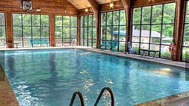 Una piscina interior con paredes de vidrio transparente, vigas de madera y un banco a lo largo de un lateral.