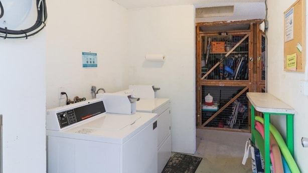 Un espace buanderie comprenant un lave-linge, un sèche-linge et un meuble de rangement en bois doté d’étagères.