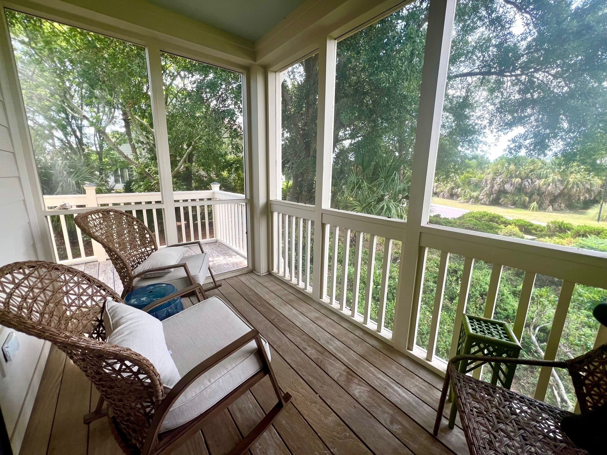 A covered porch with wicker furniture and a view of a lush garden.