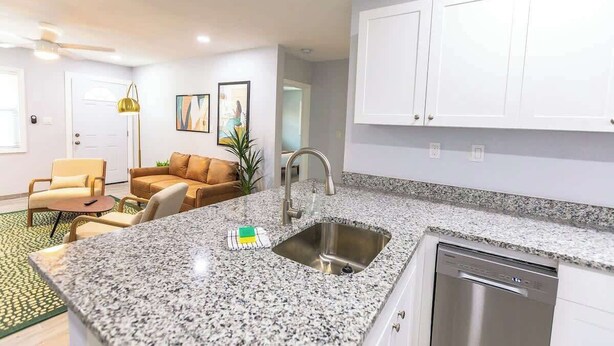 Una cocina moderna con encimeras de granito, un lavamanos de acero inoxidable y un lavavajillas integrado.