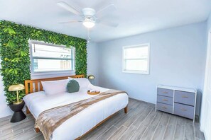 Une chambre à coucher comprenant un lit, un ventilateur de plafond, un téléviseur fixé au mur, une table de chevet et une petite table d’appoint.