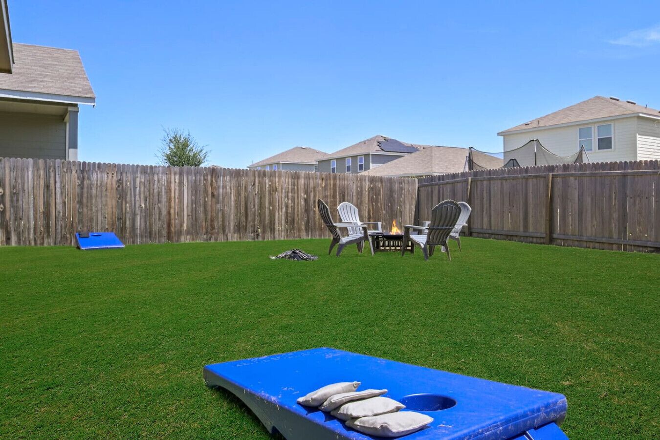 Un patio trasero con un trampolín azul, dos sillas Adirondack y un pequeño pozo de fuego.