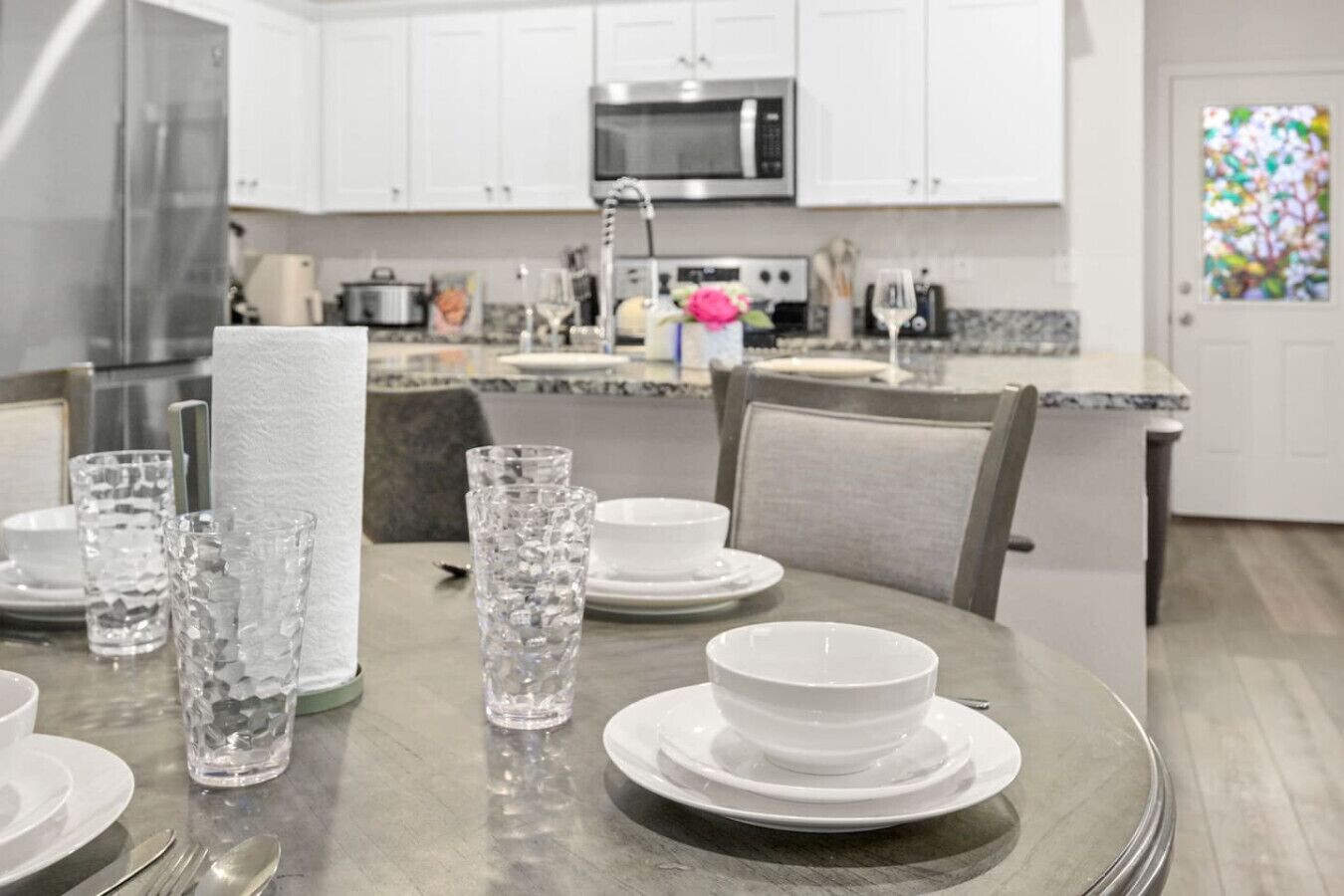 A modern kitchen with white cabinets, a stainless steel microwave, and a dining area with a round table set for four.