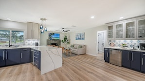 A modern kitchen with a large island, dark cabinets, and a dining area with a sofa. - Modern Spacious 3 Bedroom, 2 Bathroom Private Pool Home in Sarasota Near Siesta Key (Sarasota)