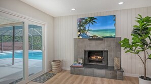 A living room with a fireplace, a pool visible through glass doors, and a large painting of a beach scene. - Modern Spacious 3 Bedroom, 2 Bathroom Private Pool Home in Sarasota Near Siesta Key (Sarasota)
