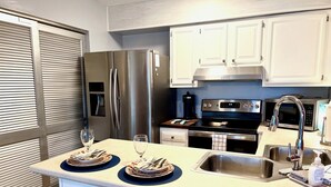 Una cocina moderna con electrodomésticos de acero inoxidable, una isla central con taburetes y muebles de cocina blancos.
