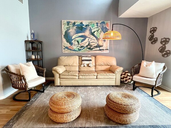 A living room with a beige sofa, two wicker chairs, a woven rug, and a wall-mounted lamp. - Top Floor Beach Retreat Tennis Courts Views 1812 (Seabrook Island)