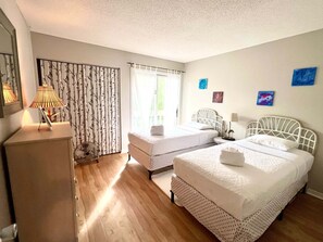 A room with two beds, a desk, a lamp, and a window with curtains. - Top Floor Beach Retreat Tennis Courts Views 1812 (Seabrook Island)