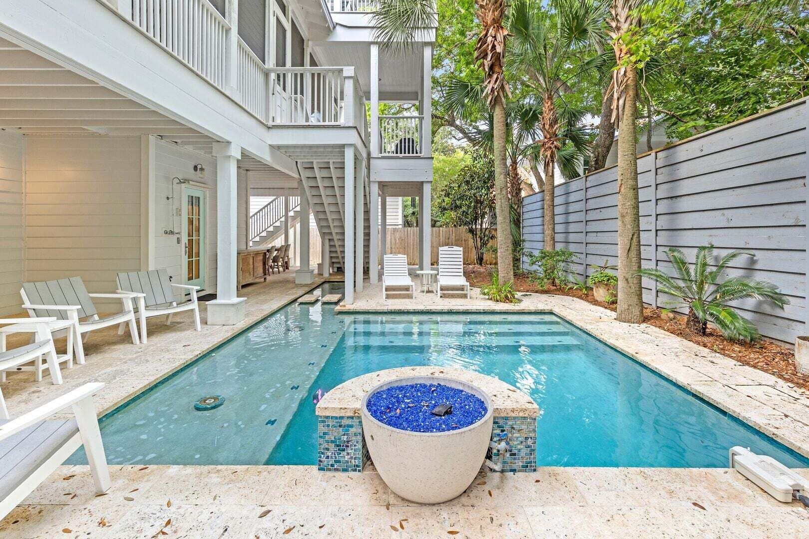 A swimming pool with lounge chairs and a hot tub, surrounded by a wooden deck and palm trees.
