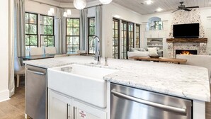 A modern kitchen with a large island, stainless steel appliances, and a built-in fireplace. - Serenity Now (Santa Rosa Beach)