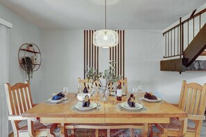 A dining area with a wooden table set for four, surrounded by chairs. A decorative hanging light fixture is above the table, and there is a staircase to the right. - Osborn (Scottsdale)