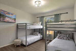 A room with bunk beds, a small stool, a painting, and a window with curtains. - Osborn (Scottsdale)