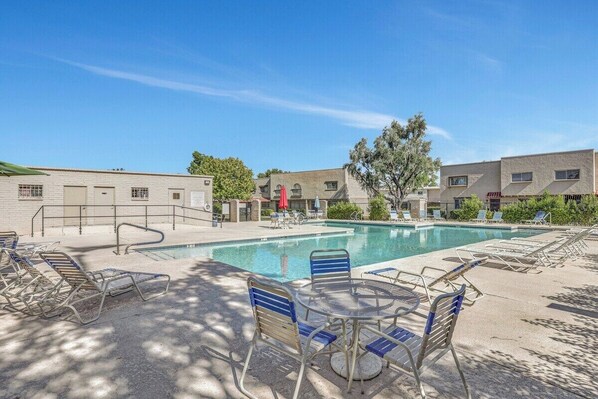A pool area with lounge chairs and a table, surrounded by buildings with a simple architectural style. - Osborn (Scottsdale)