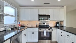 A modern kitchen with white cabinets, stainless steel appliances, and a black countertop. - Siesta Heron 7 (Siesta Key)
