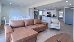 A modern living room with a sectional sofa, a coffee table, and a dining area with a white table and chairs. - Siesta Heron 7 (Siesta Key)