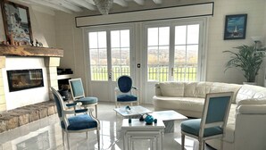 A spacious living room with a fireplace, large windows, and a white leather sofa. - Beautiful, 1h to Paris, 8-bedroom country house in soothing Normandie (Évreux)