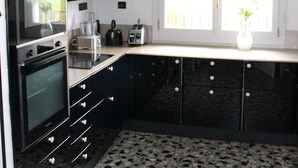 A modern kitchen with black cabinets, a built-in oven, a coffee maker, and a window with a view. - Beautiful, 1h to Paris, 8-bedroom country house in soothing Normandie (Évreux)