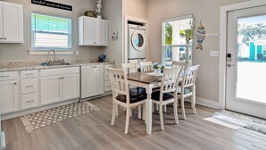 A kitchen with white cabinets, a dishwasher, a dining table with chairs, and a washing machine. - Free Bird @ The Oasis | Relaxed Coastal Cottage Retreat (Rockport)
