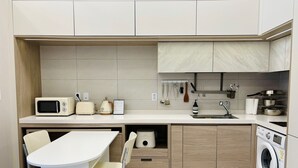 Eine kompakte Küche mit Mikrowelle, Toaster und Spüle. Ein Stuhl und ein kleiner Tisch sind vorhanden.