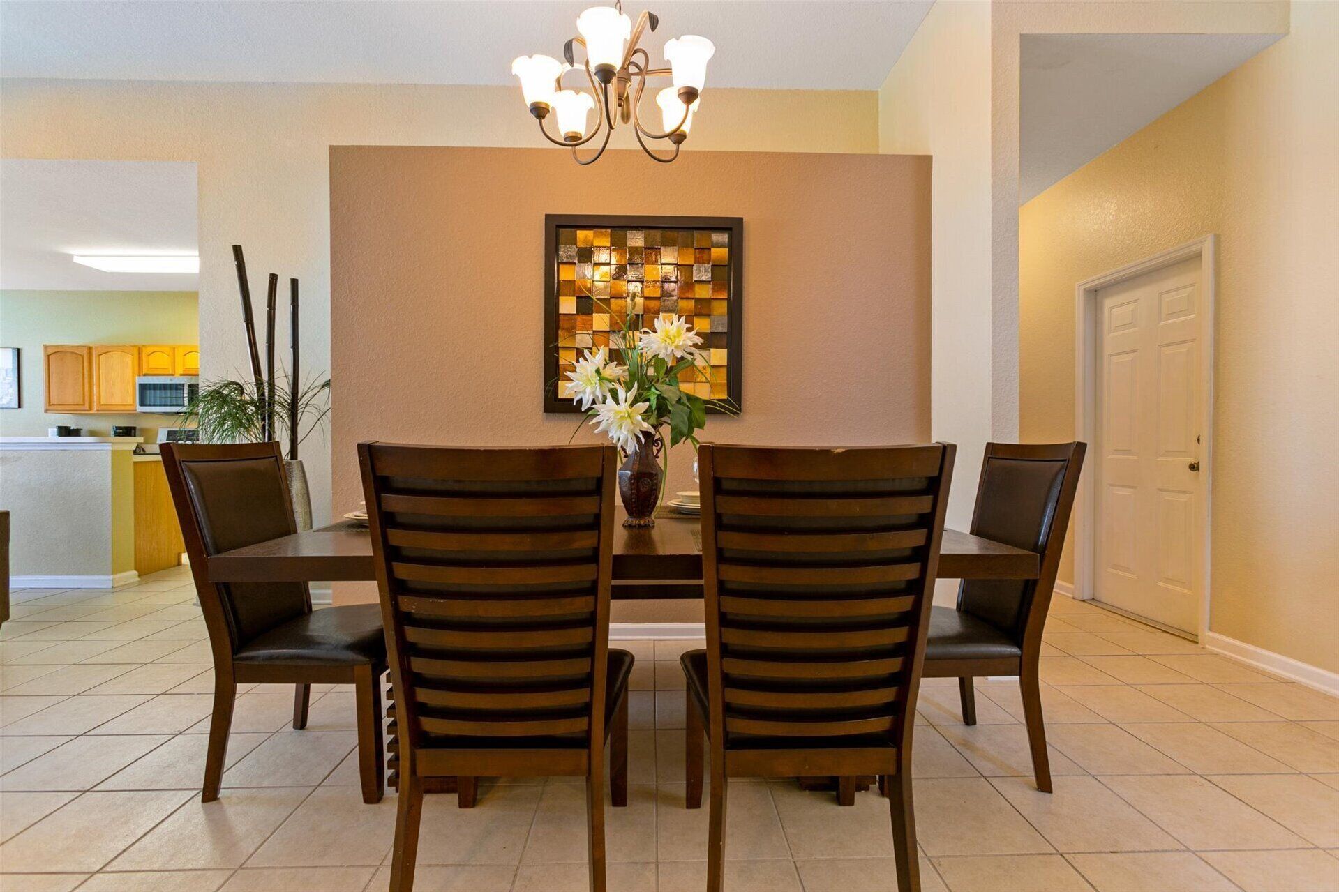 A dining area with a table, four chairs, a vase with flowers, and a wall-mounted light fixture.