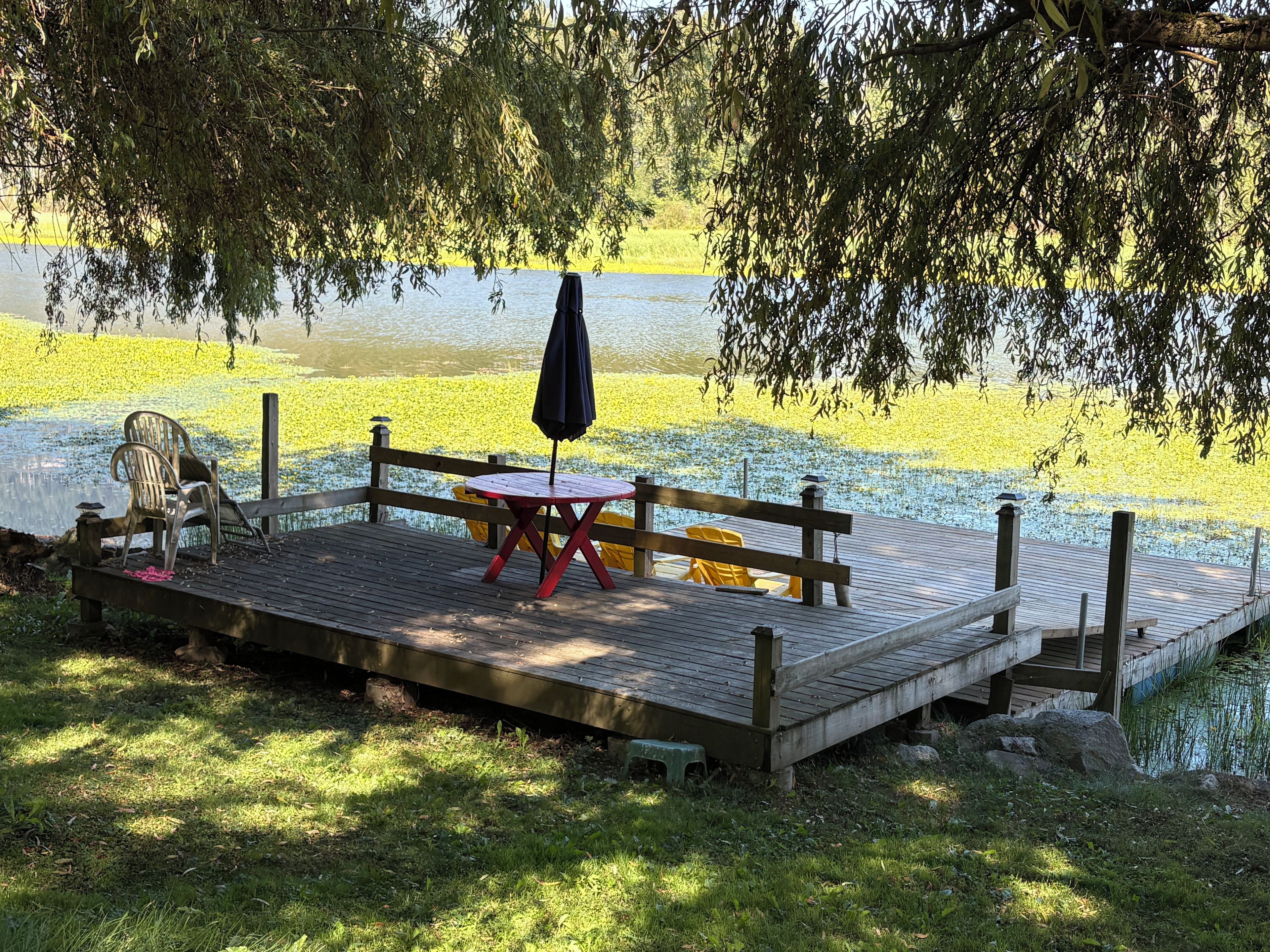 Une jetée en bois avec une table et des chaises, un banc et un parasol.