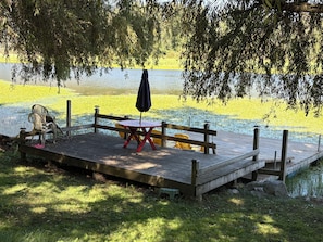 A wooden dock with a table and chairs, a bench, and an umbrella.