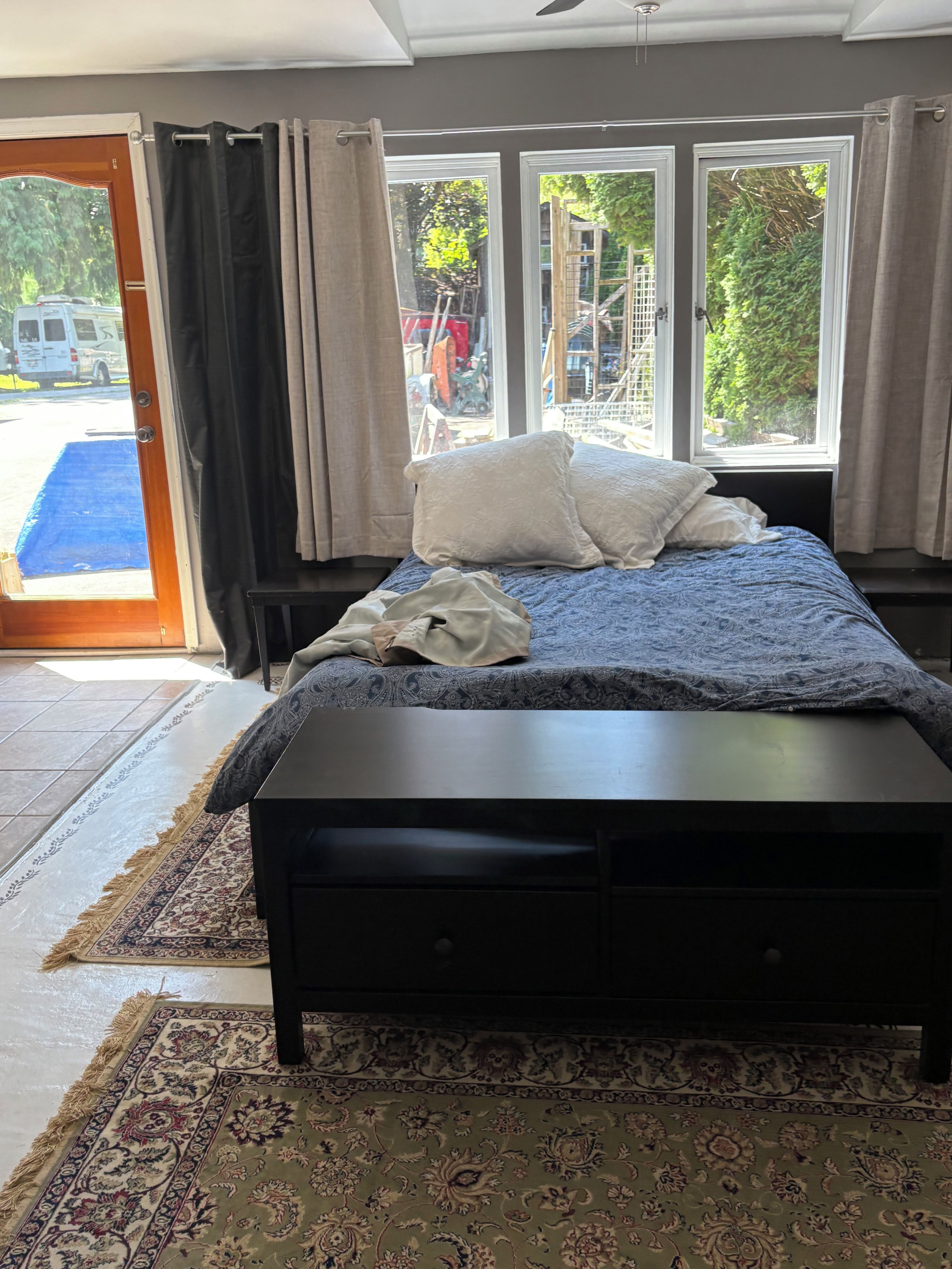 Une chambre à coucher avec un lit, une table de chevet, une fenêtre avec des rideaux et une vue sur l’extérieur.