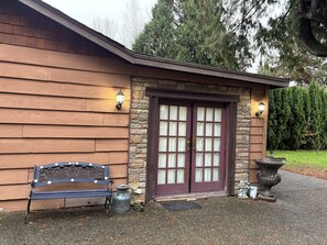A wooden building with a stone facade, a bench, a door with glass panels, and a stone planter with a squirrel figurine.