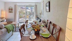 Ein Essbereich mit einem Holztisch, gedeckt für vier Personen, umgeben von Stühlen und mit Blick ins Freie durch große Fenster.