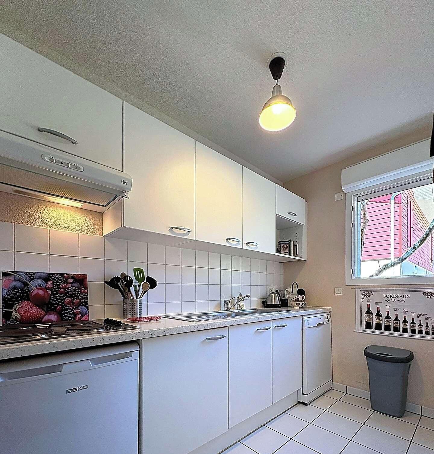 Een moderne keuken met witte kasten, een ingebouwde kookplaat en een raam met uitzicht op roze huizen.