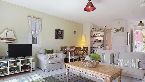 Ein Wohnzimmer mit Fernseher, Sofa, Esstisch und einem gemusterten Teppich.