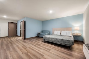 A hotel room with a bed, a chair, a desk, and a door. - Woodspring Suites Baton Rouge Airport (Baton Rouge)