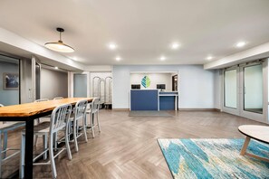A spacious room with a long wooden table and chairs, a small kitchen area, and a large window. - Woodspring Suites Baton Rouge Airport (Baton Rouge)