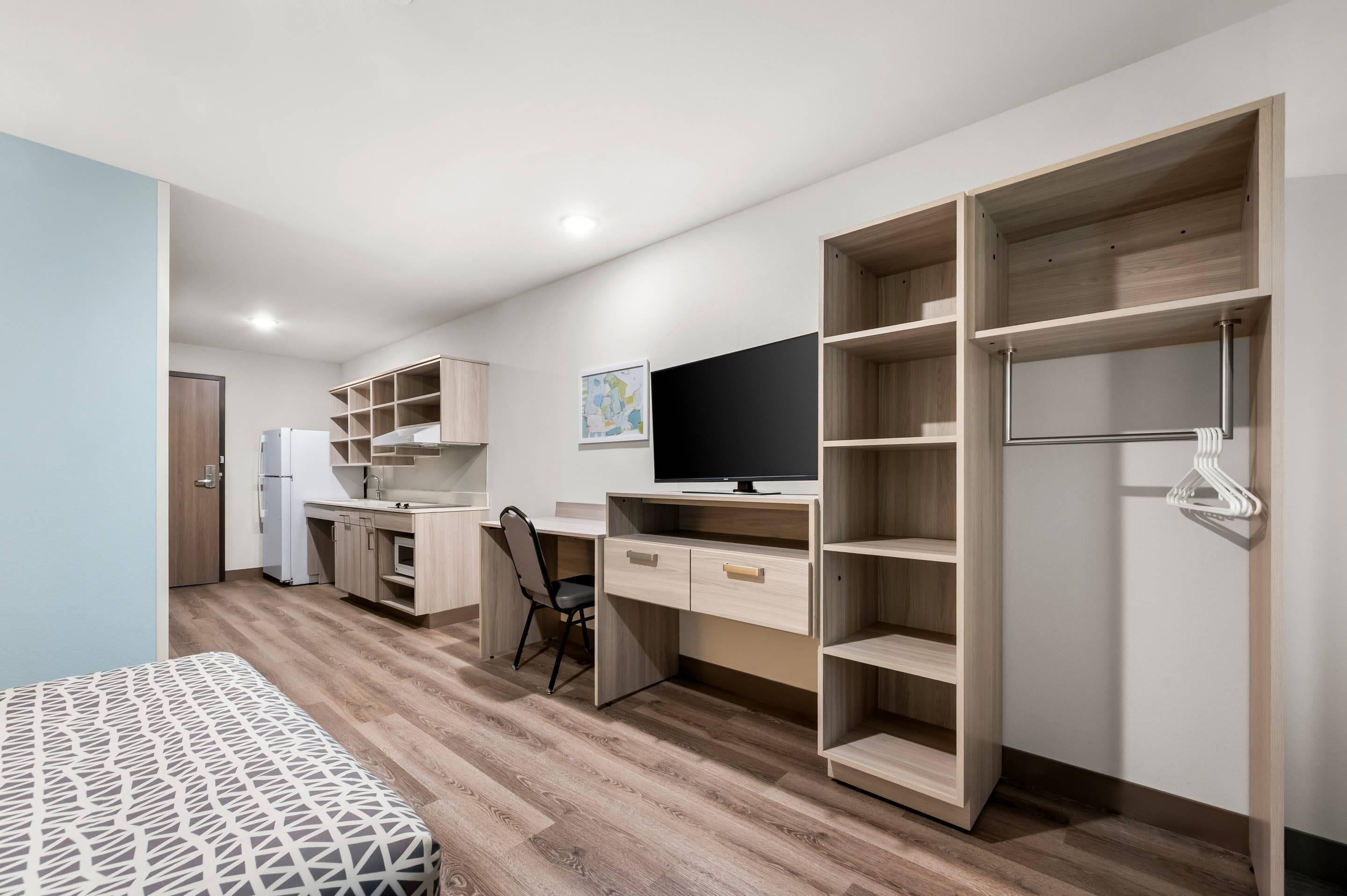 Una habitación moderna y compacta con kitchenette, una cama, un escritorio y un televisor.